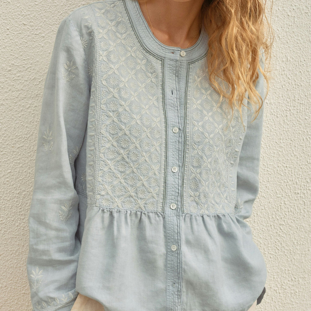 Woman wearing a light blue blouse against a beige wall