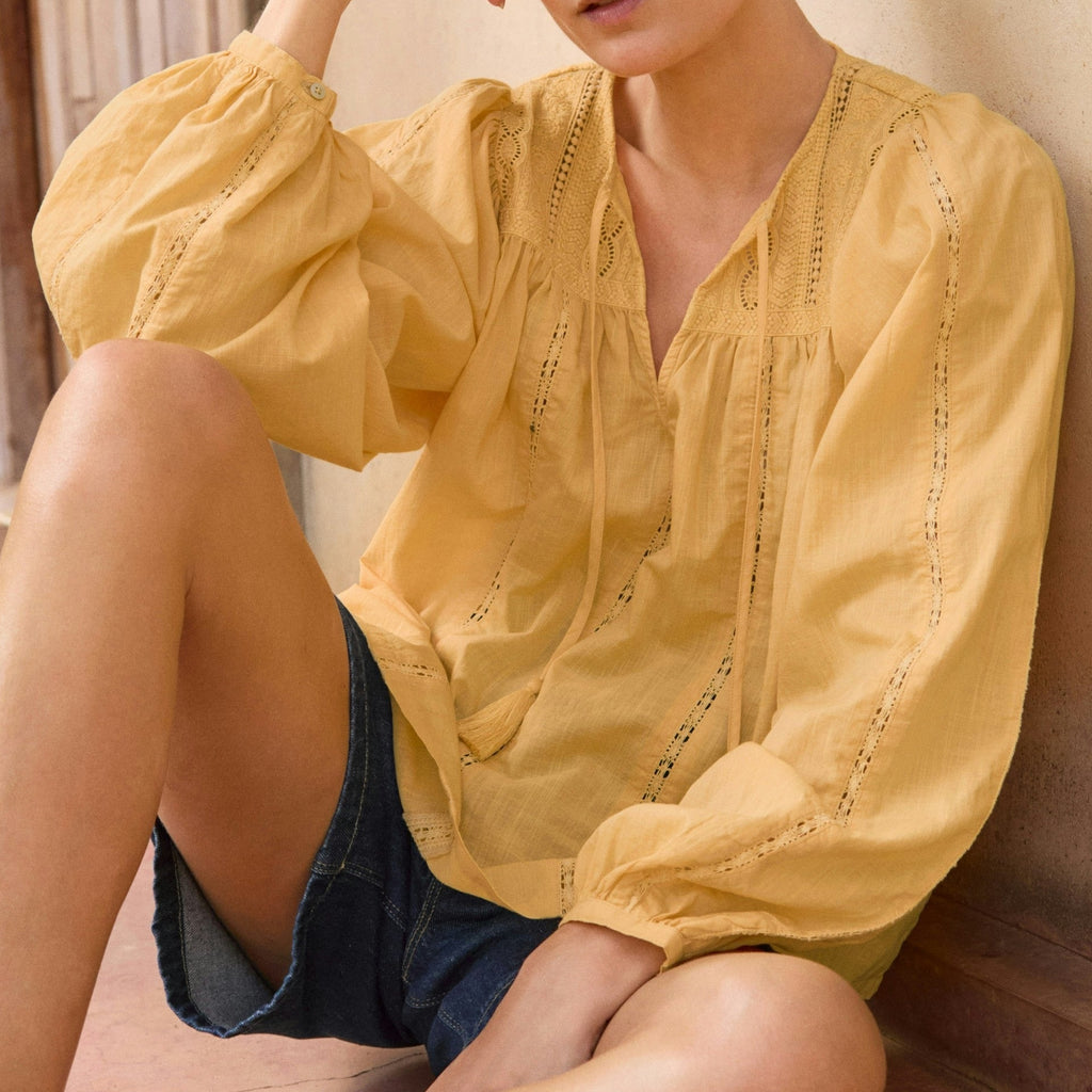 Woman wearing a yellow blouse sitting on a stone step.