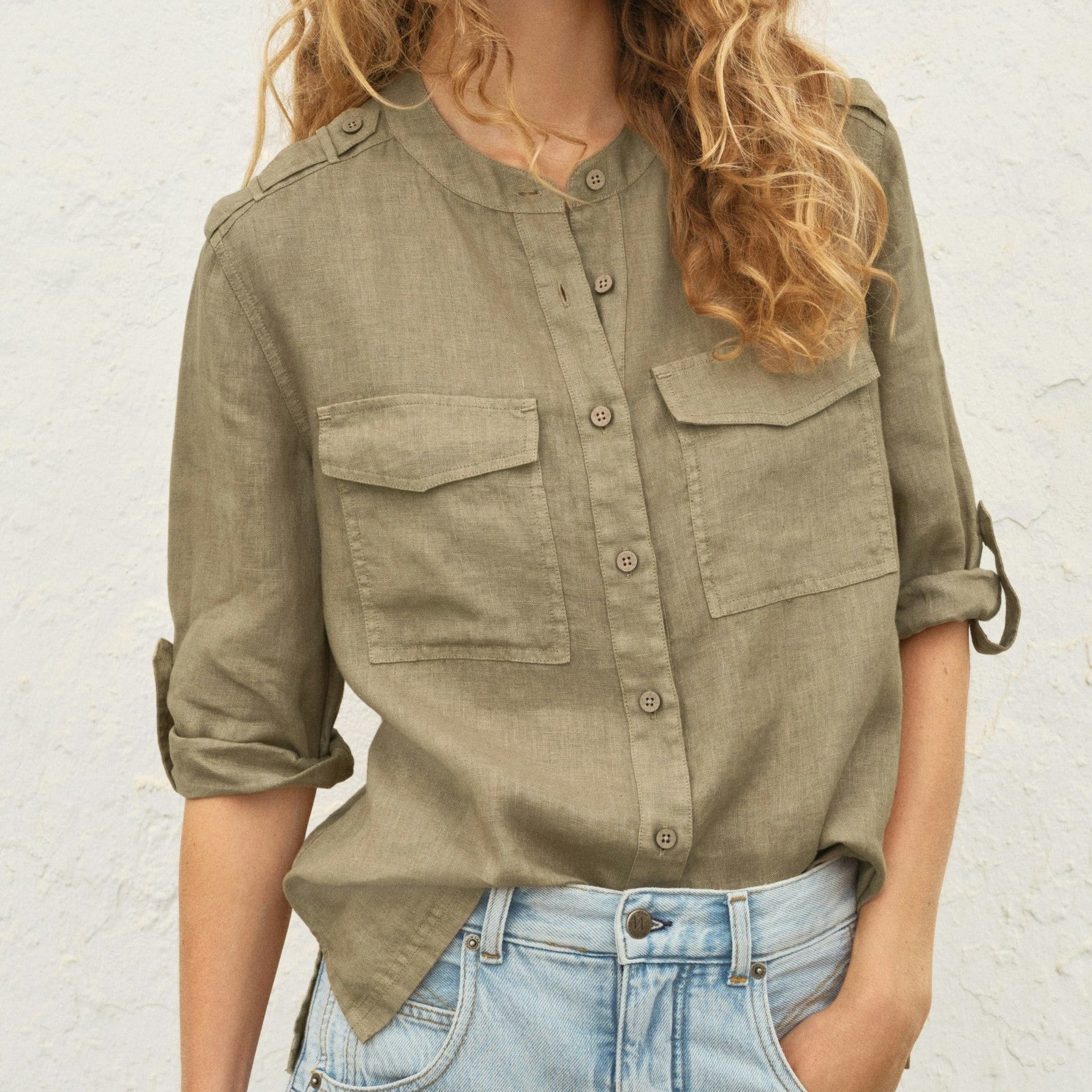 Woman wearing a green shirt and blue jeans against a white wall